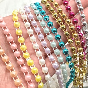 May include: A collection of multi-colored bead trim strands featuring round, glossy beads in shades of pink, yellow, white, lavender, light blue, turquoise, gold, magenta, and silver, each attached to a thin, white, flexible cord.