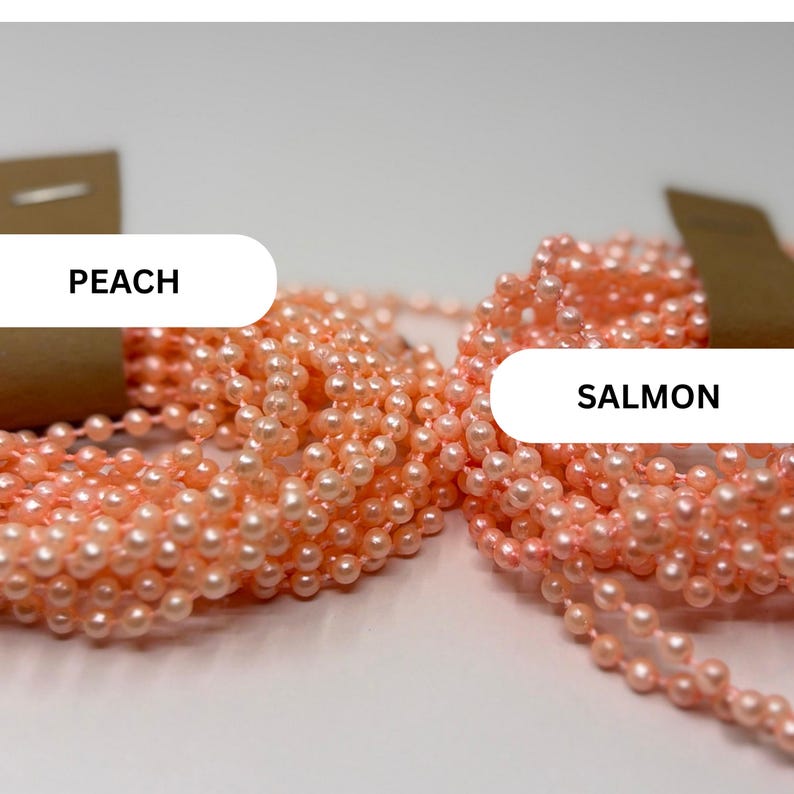 May include: Two coiled strands of ball chain, one labeled PEACH and the other labeled SALMON. Each strand consists of small, round, glossy beads in light orange and pinkish-orange hues, attached to brown cardboard tags at the ends.