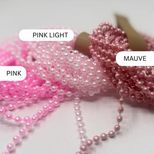 May include: Three coiled strands of small, round beads in varying shades of pink. The labels identify the colors as PINK LIGHT, PINK, and MAUVE. Each strand consists of numerous tiny, smooth, spherical beads connected in a continuous chain.