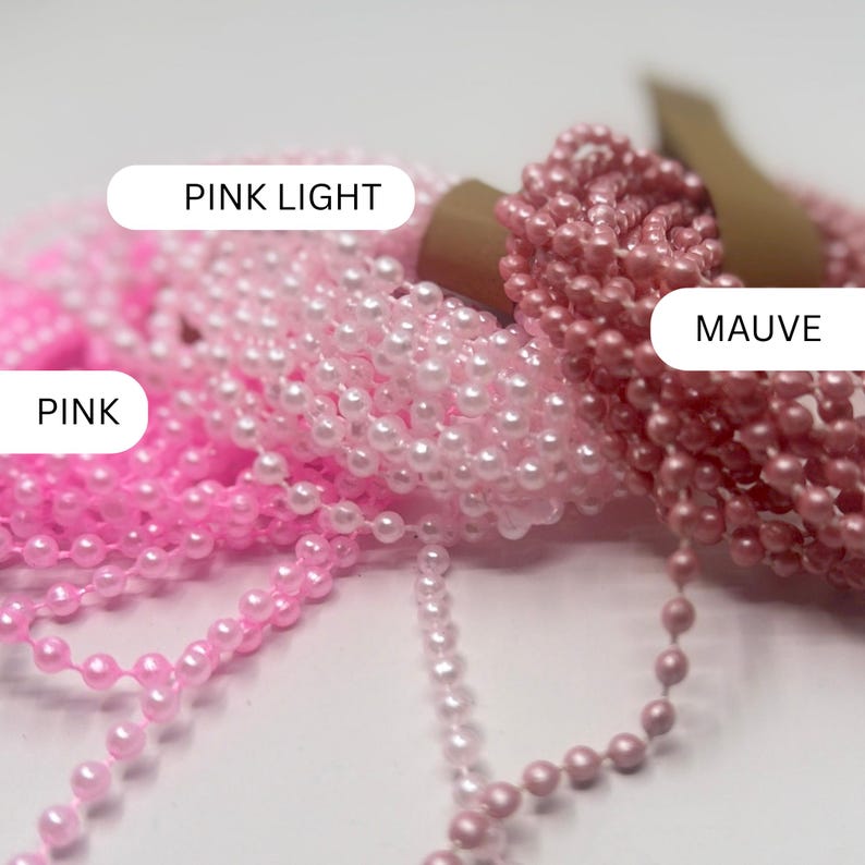 May include: Three coiled strands of small, round beads in varying shades of pink. The labels identify the colors as PINK LIGHT, PINK, and MAUVE. Each strand consists of numerous tiny, smooth, spherical beads connected in a continuous chain.