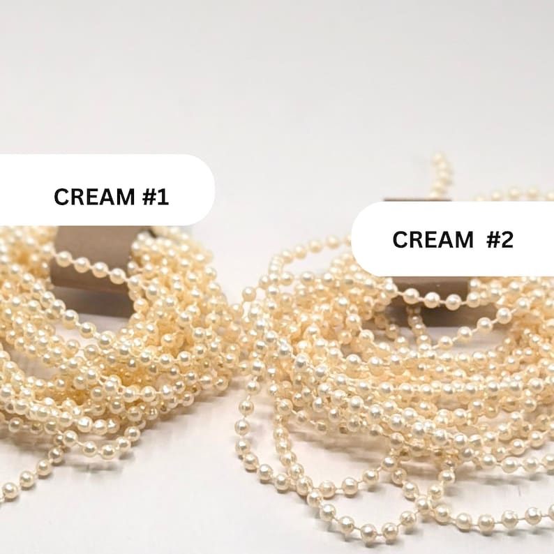 May include: Two bundles of cream-colored pearl bead strands, each wrapped around a brown cardboard holder. The left bundle is labeled CREAM #1 and the right bundle is labeled CREAM #2. The beads are small, round, and have a glossy finish.