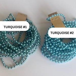 May include: Two coiled strands of ball chain, each attached to a brown cardboard tag. The left strand is labeled TURQUOISE #1 and features a deep teal blue finish. The right strand is labeled TURQUOISE #2 and features a lighter, bright sky blue finish.