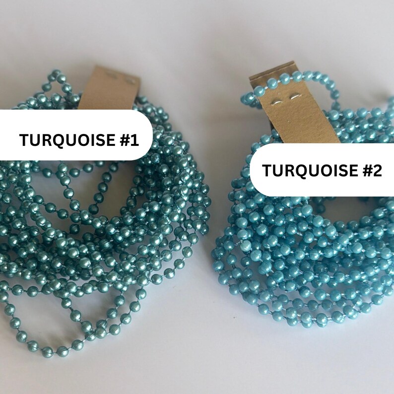 May include: Two coiled strands of ball chain, each attached to a brown cardboard tag. The left strand is labeled TURQUOISE #1 and features a deep teal blue finish. The right strand is labeled TURQUOISE #2 and features a lighter, bright sky blue finish.