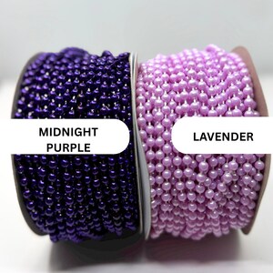 May include: Two spools of ball chain, one in midnight purple and one in lavender. Each spool features a continuous strand of small, round, glossy beads strung together, with text labels identifying the colors as MIDNIGHT PURPLE and LAVENDER.