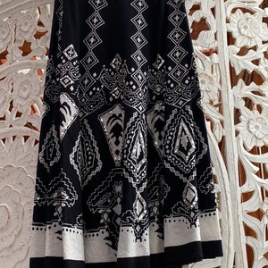 May include: A black and white patterned skirt hangs on a hanger. The skirt features a repeating geometric design with diamond and rectangular shapes. The bottom hem is white with a black border. The skirt is made of a lightweight fabric.