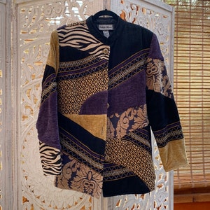 Könnte beinhalten: Patchwork-Jacke mit verschiedenen Mustern und Texturen. Sie hat Zebra-, Blumen- und geometrische Designs in Schwarz, Gold, Lila und Beige. Das Etikett lautet "Indige Moon".
