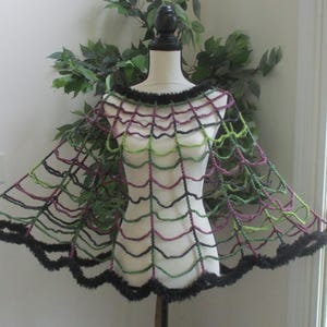 May include: A handmade Halloween cape in a spiderweb design. The cape features a black, green, and purple web pattern with a black fur trim. The cape is displayed on a mannequin.