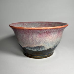 May include: A ceramic bowl with a pink, white, and black glaze. The bowl has a rounded shape and a wide rim.