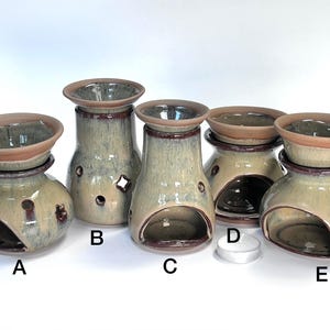 May include: A collection of five ceramic oil warmers in various shapes and sizes. Each warmer has a light green and brown glaze, with a bowl at the top and an opening for a tea light. The warmers are labeled A, B, C, D, and E.