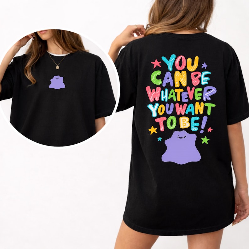May include: Black t-shirt featuring a purple blob graphic on the front and back. The back of the shirt has the text "YOU CAN BE WHATEVER YOU WANT TO BE!" in colorful letters with stars. The shirt is a comfortable, casual style.