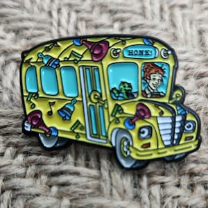 May include: A yellow school bus with a black outline and a red, white, and blue musical design. The bus has a sign that says "HONK!" and a driver with red hair and a green creature in the passenger seat.
