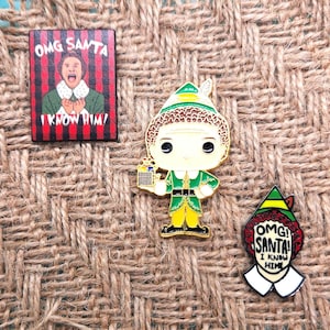 May include: Three enamel pins featuring the character Buddy the Elf from the movie Elf. The pins are all gold-colored and feature Buddy's face with the text "OMG! Santa! I know him!" on two of the pins. The third pin features Buddy holding a gift box.