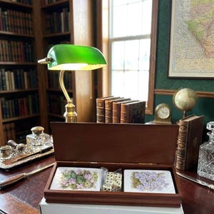 Puede incluir: Una taza de cerámica blanca con un asa negra y el texto "But First, Coffee" en negrita negra. La taza se encuentra sobre un fondo borroso, sugiriendo un ambiente acogedor.