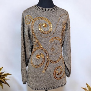 May include: A silver sweater with a gold sequined design of swirling lines. The sweater has long sleeves and a round neckline.
