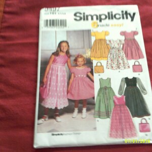 Könnte beinhalten: Simplicity-Schnittmuster für Mädchenkleider. Das Schnittmuster enthält fünf verschiedene Kleiderschnitte, darunter ein gelbes Kleid, ein Blumenkleid, ein grünes Kleid, ein schwarzes Kleid und ein rosa Kleid. Das Schnittmuster enthält auch Anleitungen für die Herstellung einer passenden Handtasche.
