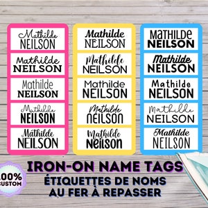 May include: Five sets of iron-on name tags with the name "Mathilde Neilson" printed in black on a white background. The tags are on pink, yellow, and blue backgrounds. The text "IRON-ON NAME TAGS" is printed in black on a white background. The text "ÉTIQUETTES DE NOMS AU FER À REPASSER" is printed in black on a white background. A 100% custom label is in the bottom left corner.