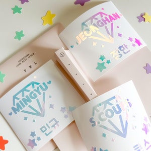 May include: Four holographic diamond-shaped stickers with the names of K-pop idols: JeongHan, Mingyu, S.Coups, and the Korean text for their names. The stickers are on a pink and white background with small holographic stars.