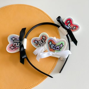 May include: Three black headbands with colorful heart-shaped hair clips. The clips have Korean text that reads "pretty", "love", and "cute".