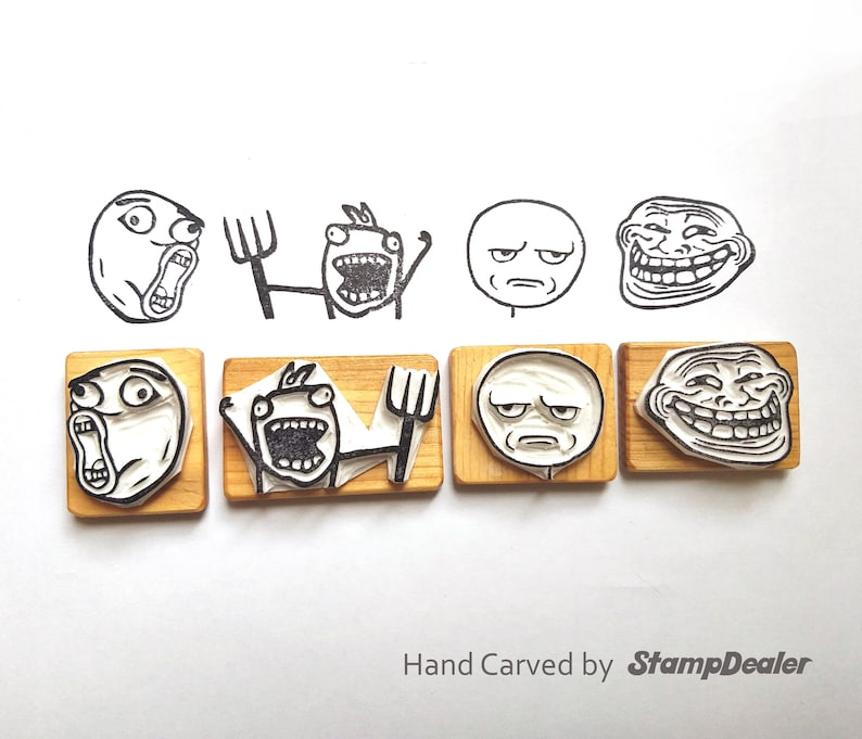 May include: Six wooden stamps featuring various internet meme faces, including Trollface,  Forever Alone, and  'You're doing it wrong'. The stamps are hand-carved and have a light brown color. The text 'Hand Carved by StampDealer' is printed below the stamps.