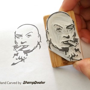 May include: A hand-carved rubber stamp featuring a black and white illustration of a man with a moustache, smoking a cigarette. The stamp is mounted on a wooden block. The text "Hand Carved by StampDealer" is printed below the image.