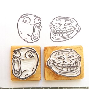 May include: Four wooden blocks with different troll face rubber stamps. The stamps are black and white and depict different troll face expressions.