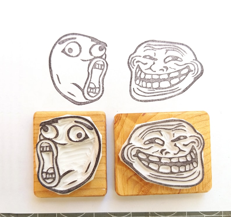 May include: Four wooden blocks with different troll face rubber stamps. The stamps are black and white and depict different troll face expressions.