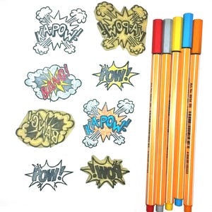 May include: Image features comic book speech bubbles with words like "KAPOW!" and "POW!" in various colours. Next to them are six orange pens with coloured tips, including red, grey, yellow, blue, and orange.