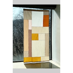 以下が含まれることがあります： 茶色、ベージュ、オレンジの色合いの正方形と長方形が幾何学的に配置された壁掛けのタペストリーです。