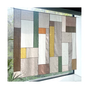 以下が含まれることがあります： 茶色、ベージュ、緑、黄色の様々な色合いで幾何学模様が施された壁掛けのタペストリー。タペストリーは織物で作られており、パッチワークスタイルです。