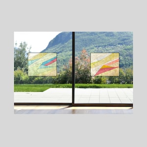 May include: Two stained glass window decals with geometric patterns in shades of yellow, blue, red, and white. The decals are placed on a glass door with a view of a green grassy area and a mountain in the background.