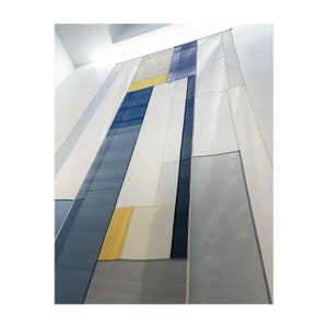 May include: A large abstract wall hanging made of different shades of blue, gray, and yellow fabric. The fabric is sewn together in a geometric pattern.