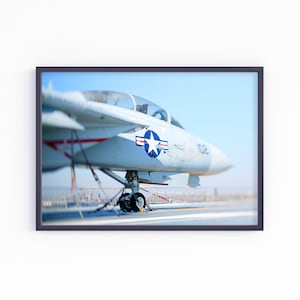 Könnte beinhalten: Ein weißes Kampfflugzeug mit einem blauen und weißen Stern an der Seite steht auf einer Landebahn. Das Flugzeug befindet sich auf dem Deck eines Flugzeugträgers.