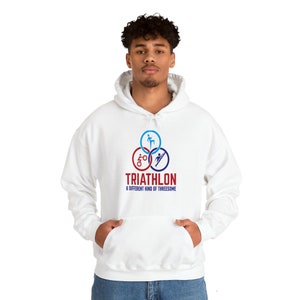 Peut inclure: Sweat-shirt à capuche blanc avec un logo de triathlon rouge, bleu et blanc. Le logo présente trois icônes représentant la natation, le cyclisme et la course à pied. Le texte sous le logo indique "TRIATHLON A DIFFERENT KIND OF THREESOME".