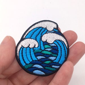 May include: Blue and white embroidered iron-on patch of a stylized wave.