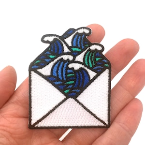 May include: An embroidered iron-on patch featuring a white envelope with blue and green waves bursting out of it.