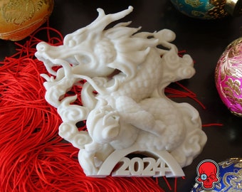May include: White ceramic dragon figurine with the year 2024 printed on the base. The dragon is curled up with its head facing the left. The figurine is sitting on a red tassel.