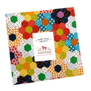 May include: A square fabric bundle with a colorful patchwork design of hexagons in various colors and patterns. A white label in the center reads "RUBY STAR SOCIETY" and "eatnap" with a pink cat illustration. The fabric is likely for quilting or crafting.