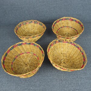 May include: Four woven wicker baskets with red and green trim. The baskets are round and have a slight curve to them. They are all empty and sitting on a grey surface.