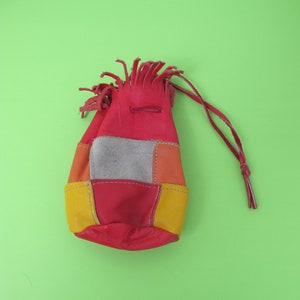 Könnte beinhalten: Ein kleiner roter Lederbeutel mit Kordelzug. Der Beutel besteht aus verschiedenen Lederstücken in verschiedenen Farben, darunter Gelb, Orange und Grau. Der Beutel hat oben einen Fransenbesatz.
