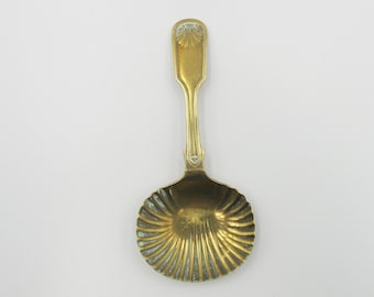 May include: A gold-colored metal spoon with a decorative, scalloped bowl and a simple, ornate handle.