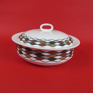 Puede incluir: Tazón de servir de cerámica blanca con tapa. El tazón tiene un patrón geométrico en marrón, rojo y negro. La tapa tiene una pequeña manija.