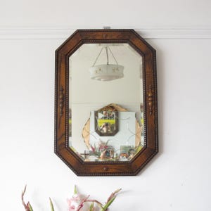 May include: An octagonal wall mirror featuring a dark brown wooden frame with decorative beaded edges and small vertical spindle accents on the sides. The glass has a beveled edge, and the frame includes small circular wooden details at the top and bottom.