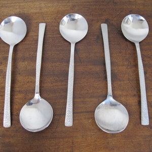 May include: Five silver spoons with textured handles. The spoons are arranged in a row on a wooden surface.