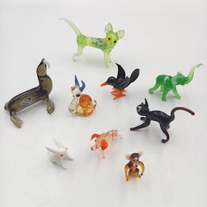 May include: A collection of small, colorful glass animal figurines. The assortment includes a seal, a cat, a dog, a bird, an elephant, a snail, a rabbit, a monkey, and a small dog. Each figurine is uniquely colored and detailed.