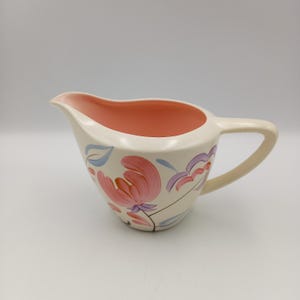 Può includere: Crema in ceramica color crema con interno pesca e manico. L'esterno è decorato con disegni floreali rosa, viola e blu. Un pezzo classico per servire panna o salse.
