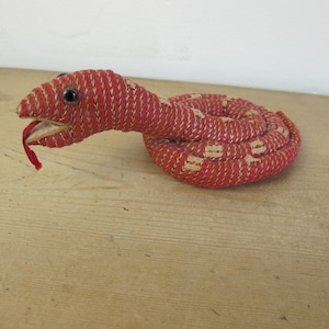 May include: A red and cream fabric snake toy. The snake is coiled and has a small black eye.