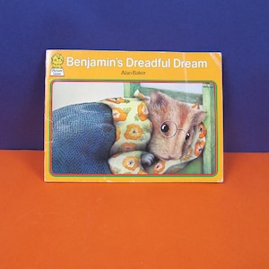 Könnte beinhalten: Ein gelbes Buch mit einem Bild eines Hamsters, der eine Brille trägt und eine Blumendecke auf dem Cover hat. Der Titel des Buches lautet "Benjamin's Dreadful Dream" von Alan Baker.