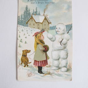 ビンテージのクリスマス ポストカード - ダックスフントと雪だるまを持つ女の子 - 雪の降るお祭りのシーン