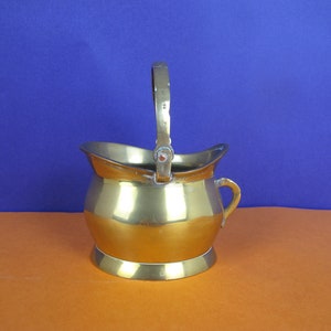 May include: A small, gold-coloured brass bucket with a handle. The bucket has a rounded bottom and a slightly flared top.