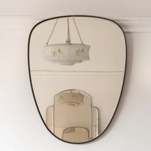 Op de afbeelding: Een decoratieve ovale spiegel met een zwart frame dat een witte plafondlamp met een bloemenmotief reflecteert.